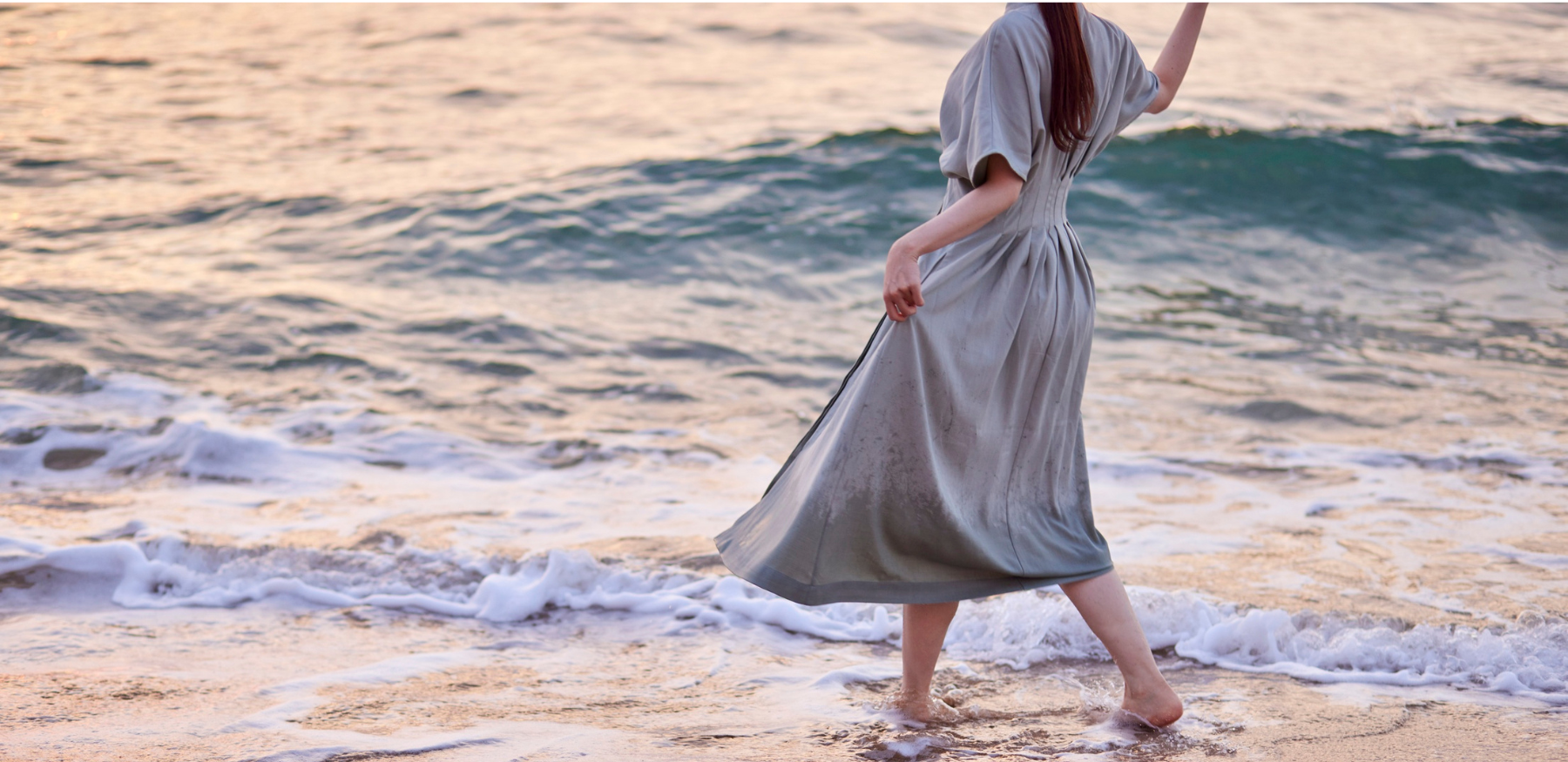 Woman in a flowing white beach dress walking by the ocean at sunset