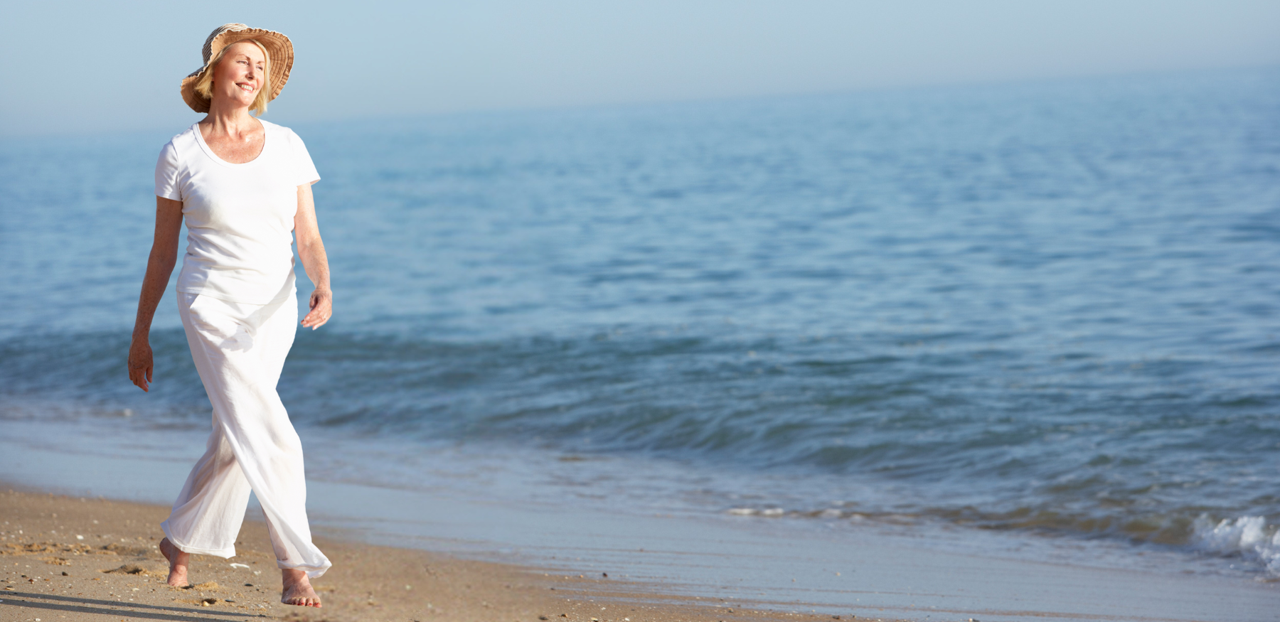 Woman in white linen beach pants walking by the sea
